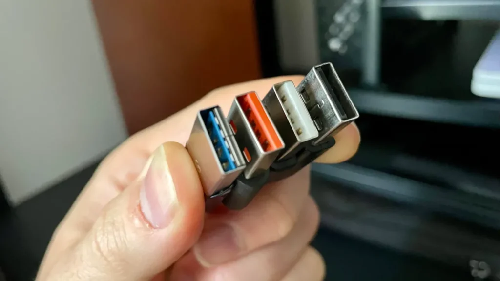 Ruka drži tri USB konektora sa plavim, crvenim i crnim unutrašnjim delom koji ilustruju razlike između USB portova