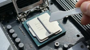 Krupni plan nanošenja termalne paste u obliku linije na Intel Core i9 procesor, sa belom plastičnom špatulom u ruci spremnom za razmazivanje.